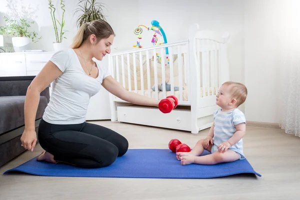 Schöne junge Mutter macht Fitness und gibt ihr Hanteln — Stockfoto