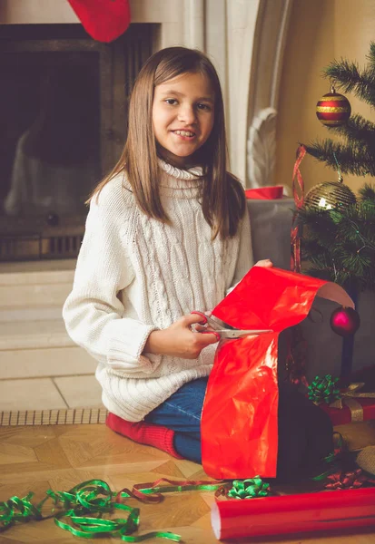 Chica feliz sentada en la chimenea y envolviendo regalos de Navidad — Foto de Stock