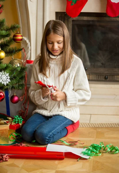 Meisje zit bij de kerstboom en snijden sneeuwvlokken uit dec — Stockfoto