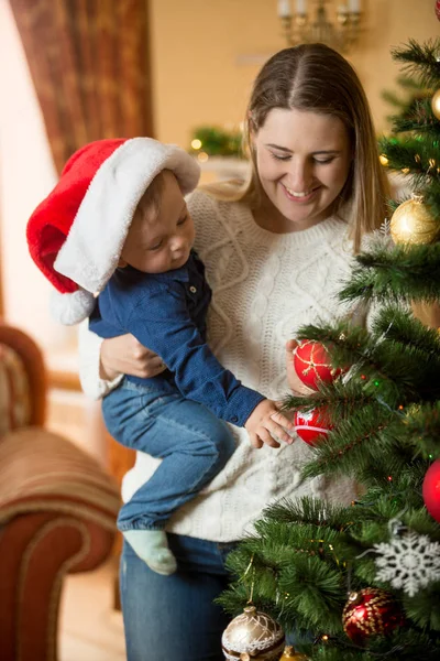 Šťastná mladá matka mazlení její chlapeček v Santa čepici na Vánoce — Stock fotografie