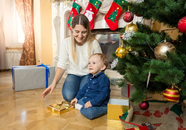 Mother sitting with her baby son on floor at living room next to — Stock Photo, Image