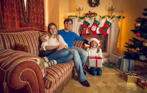 Feliz familia joven con hija posando en la sala de estar con fuego —  Fotos de Stock