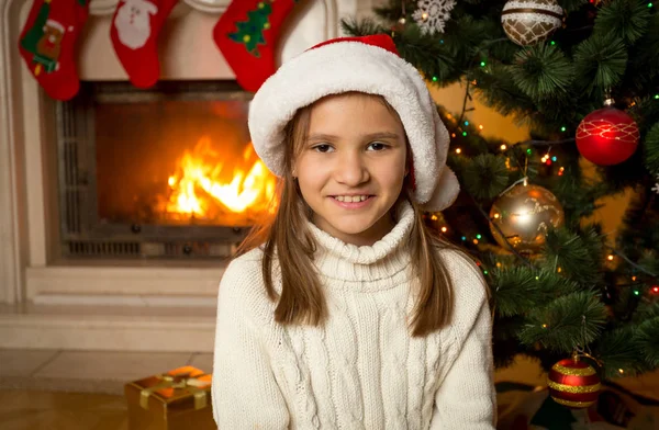 10 years old girl in Santa hat sitting next to fireplace and dec — Stock Photo, Image