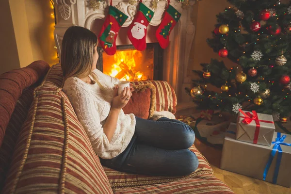 Kvinnan avslappnande av den öppna spisen och julgran med kopp t — Stockfoto