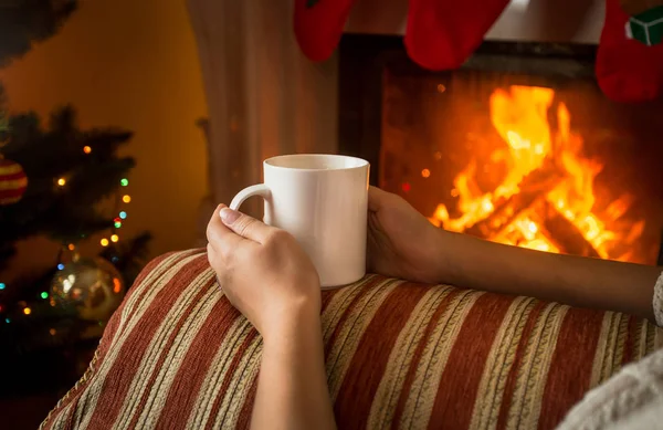Image of woman sitting on sofa by the fireplace and holding cup — Stock Photo, Image