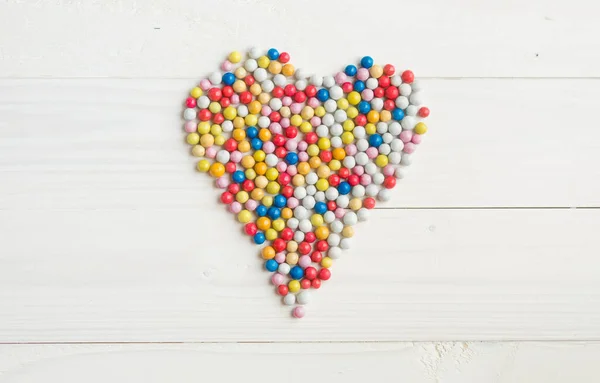Doces redondos coloridos que jazem em forma de coração em madeira branca b — Fotografia de Stock