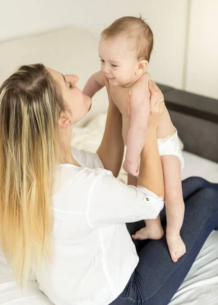 Hermosa joven madre sentada en la cama con su hijo de 6 meses —  Fotos de Stock