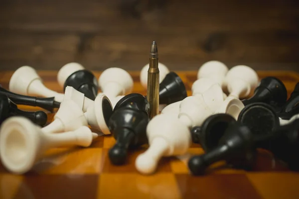 One riffle bullet on chessboard among lying chess pieces — Stock Photo, Image