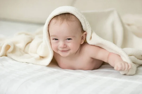 Cute cheerful baby lying under blanket on bed