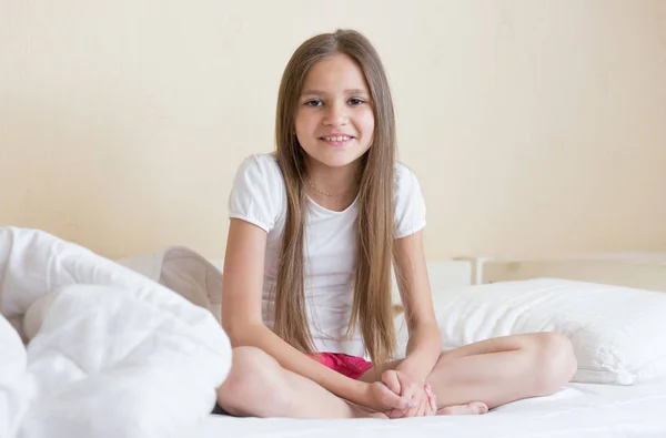 Улыбающаяся девушка с длинными темными волосами сидит на кровати — стоковое фото