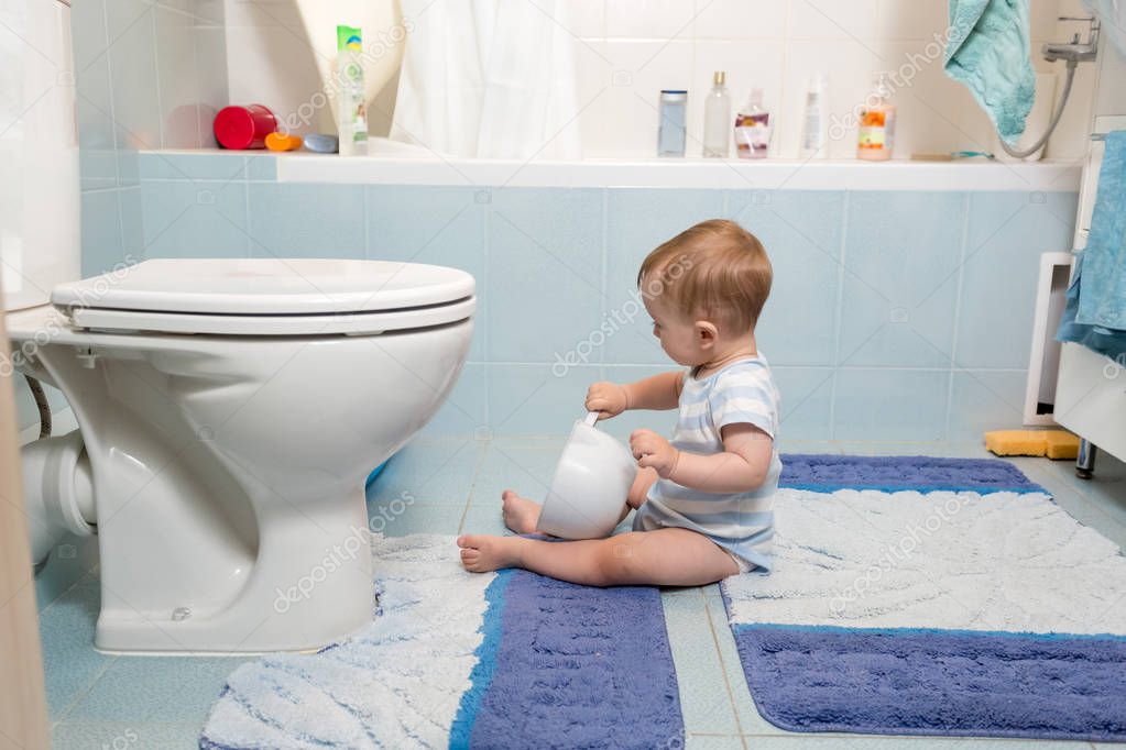 Adorable baby boy sitting on floor at bathroom and playing with 