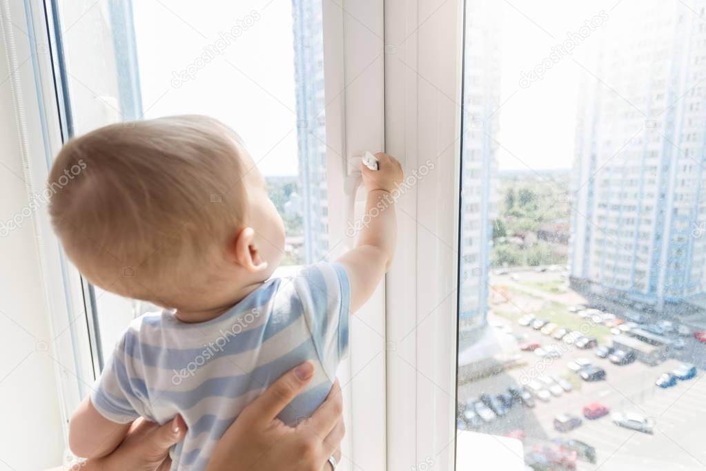 Mother holding baby boy while he is looking outside through wind