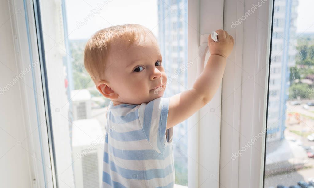 Baby boy pulling by the window handle. Concept of child in dange