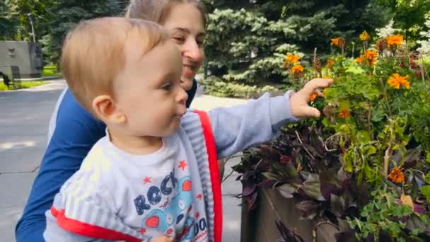 Porträt eines niedlichen Jungen mit Mutter, die Blumen im Garten riecht — Stockvideo