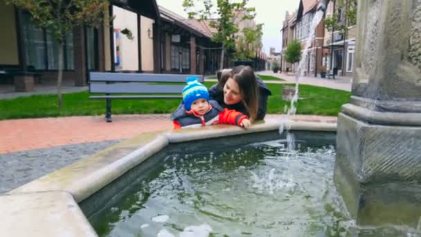 Ładny chłopczyk z matką, stojąc przy fontannie na ulicy — Wideo stockowe