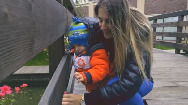 Feliz joven madre de pie en el puente de madera con su hijo bebé — Vídeos de Stock
