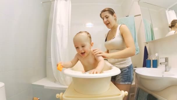 Cute active baby boy bathing with young smiling mother — Stock Video