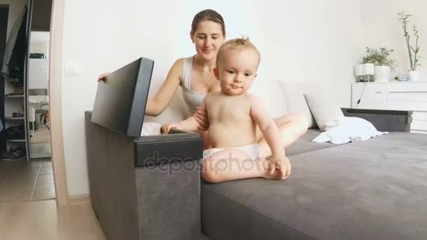 Cute baby boy sitting on sofa with mother and exploring bedside table — Stock Video