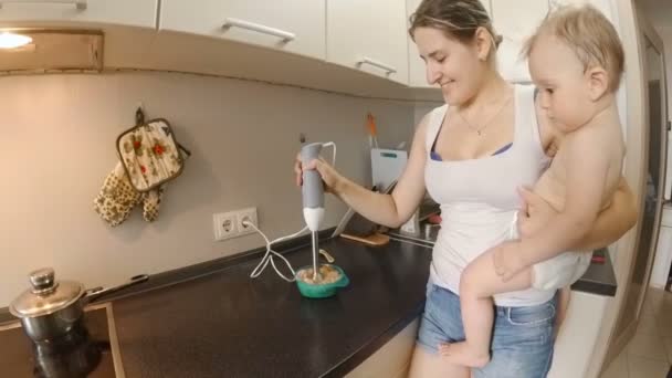 Slow motion-film av ung mor med sin baby matlagning på kök — Stockvideo