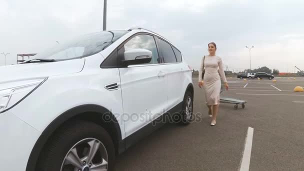 Hermosa mujer dejando vacío carrito de compras en el estacionamiento y sentado en el coche — Vídeos de Stock