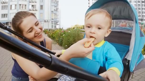 Imádnivaló baba fiú ül a babakocsi, és eszik süti — Stock videók