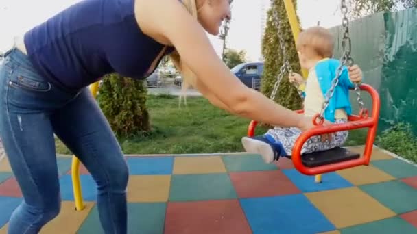 Slow motion footage of young mother swinging her baby son in swing at playground — Stock Video