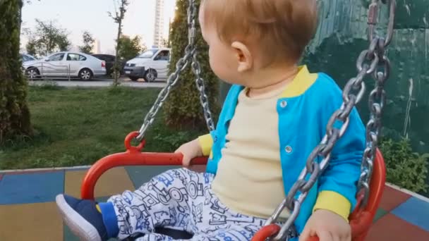 Slow-motion video van schattige babyjongen rijden op keten schommel in Speeltuin — Stockvideo