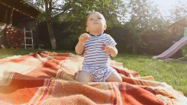 Imágenes 4K de un lindo bebé sentado en una manta en el jardín — Vídeo de stock