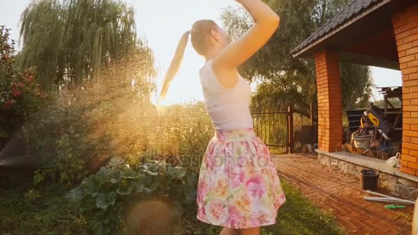 Медленная съемка молодой смеющейся женщины, танцующей под водой из садового шланга на закате — стоковое видео