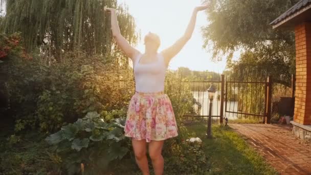 Vídeo en cámara lenta de la feliz mujer sonriente bajo el agua salpicando de aspersor de jardín al atardecer — Vídeo de stock