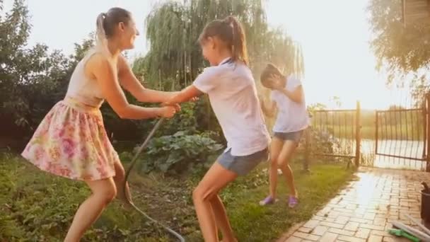 Imágenes en cámara lenta de feliz familia alegre salpicaduras de agua de la tubería de manguera en el jardín — Vídeos de Stock