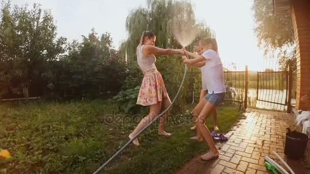 일몰에 정원 호스에서 물이 튀는 행복 한 가족 — 비디오