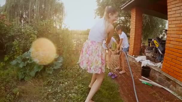 Filmato al rallentatore di allegra giovane famiglia che gioca in giardino e spruzza acqua — Video Stock