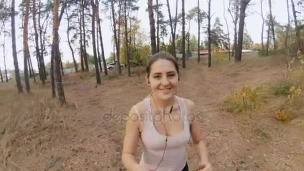 4K видео с красивой молодой женщиной, бегающей в лесу и снимающей видео на селфи-палку — стоковое видео