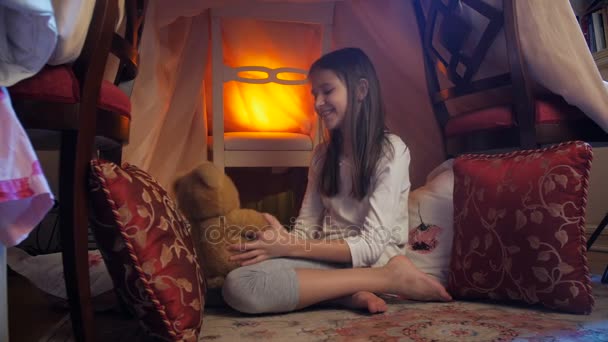 4k видео милой девушки, сидящей в палатке в спальне и обнимающей большого плюшевого мишку — стоковое видео