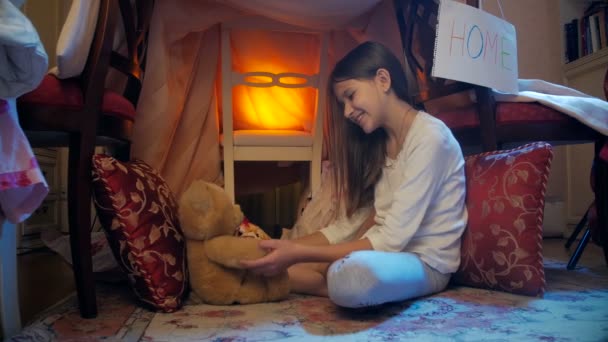 4к-кадр милой девушки в пижаме, играющей с плюшевым медведем в самодельном домике — стоковое видео