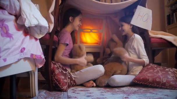 4k видео двух девушек в пижаме, играющих с плюшевым мишкой в самодельной палатке в спальне — стоковое видео