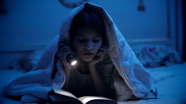 Schattig meisje onder de deken op bed lezen boek — Stockvideo