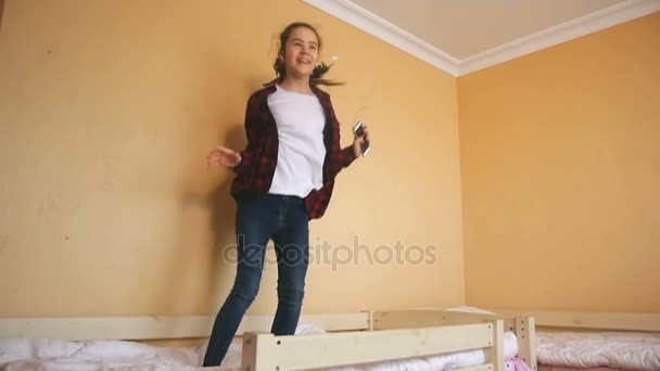 Imágenes en cámara lenta de adolescentes felices escuchando música en el reproductor y saltando en la cama — Vídeos de Stock