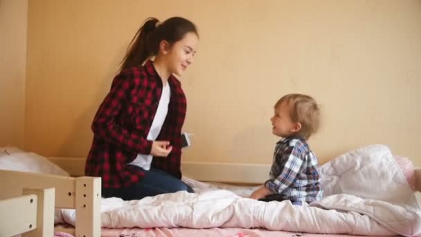 幸せな幼児の少年と 10 代の少女ダンスとベッドにジャンプのスロー モーション ビデオ — ストック動画