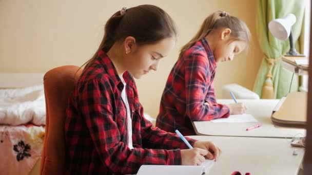 4 k beelden van twee zusters schrijven in notitieboekjes met pennen achter bureau op slaapkamer — Stockvideo