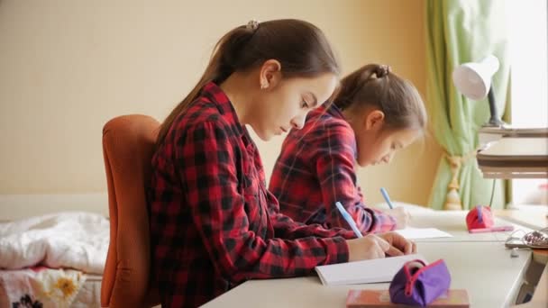 4k видео двух девочек, делающих домашнее задание за длинным столом дома — стоковое видео