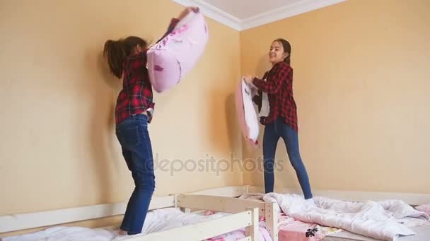 Slow motion záběry dvou veselých dívek bojuje s polštáři na posteli — Stock video