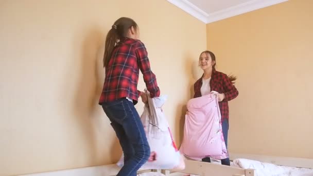 Vídeo en cámara lenta de dos hermanas felices saltando en la cama y luchando con almohadas — Vídeo de stock