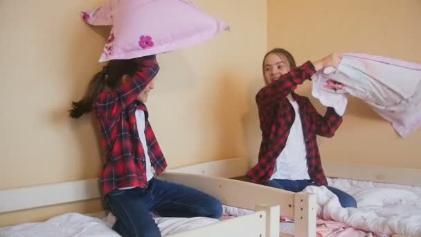 Slow motion video av två glada tjejer sitter på sängen och slåss med kuddar — Stockvideo