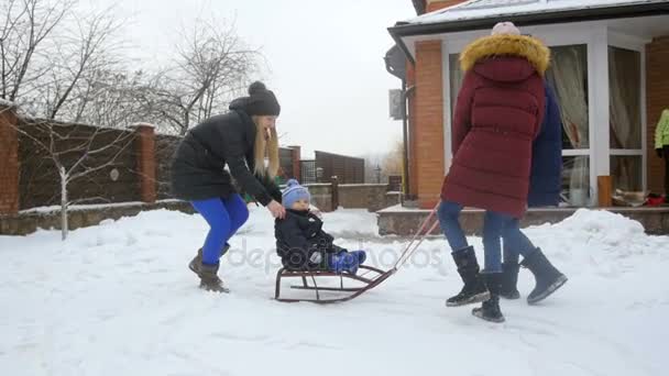 Slow motion video of family riding baby boy on sleds at house backyard — Stock Video