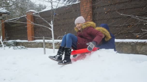 活泼开朗的女孩骑雪橇在房子后院的慢动作视频 — 图库视频影像