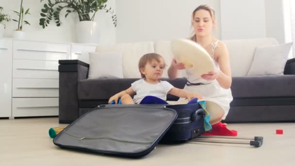 Happy young mother with her toddler son packing suitcase for summer vacation — Stock Video