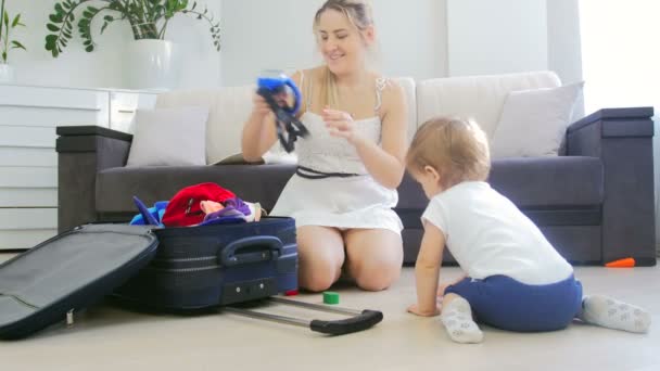 Feliz mujer sonriente con adorable bebé niño maleta de embalaje para las vacaciones de verano — Vídeo de stock