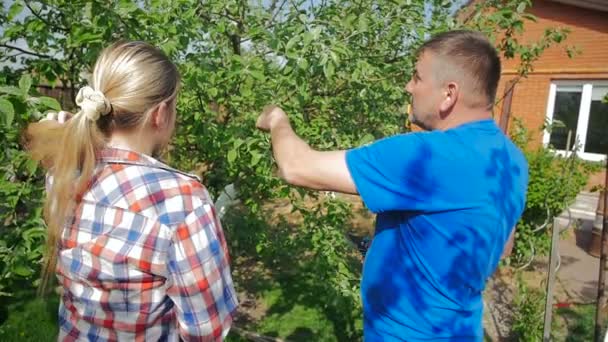 Filmagem em câmera lenta do homem sênior ensinando sua filha adulta no quintal do pomar — Vídeo de Stock